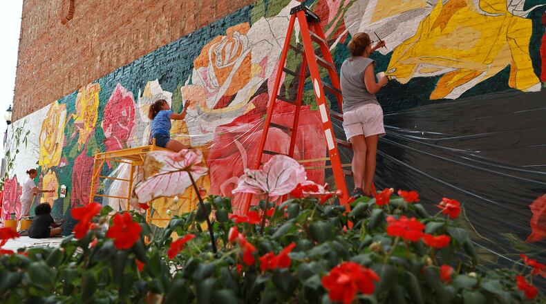 Members of Project Jericho work with artist Mariah Kaminsky to create the Rose City Mural in on the side of a building downtown Springfield Friday. The mural harkens back to when Springfield was called the Rose City because it produced more roses than anywhere else. BILL LACKEY/STAFF