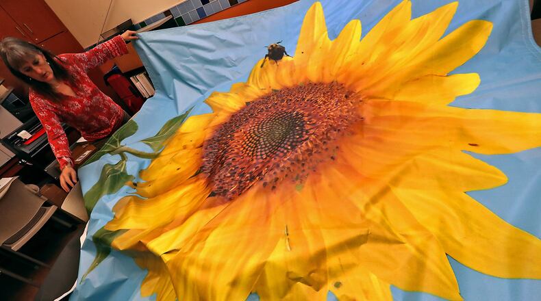 Bonnie Martens, program manager at the Clark County Solid Waste District, unfolds the mural that will be hung on the side of a building near the sunflower fields Euclid Avenue. BILL LACKEY/STAFF