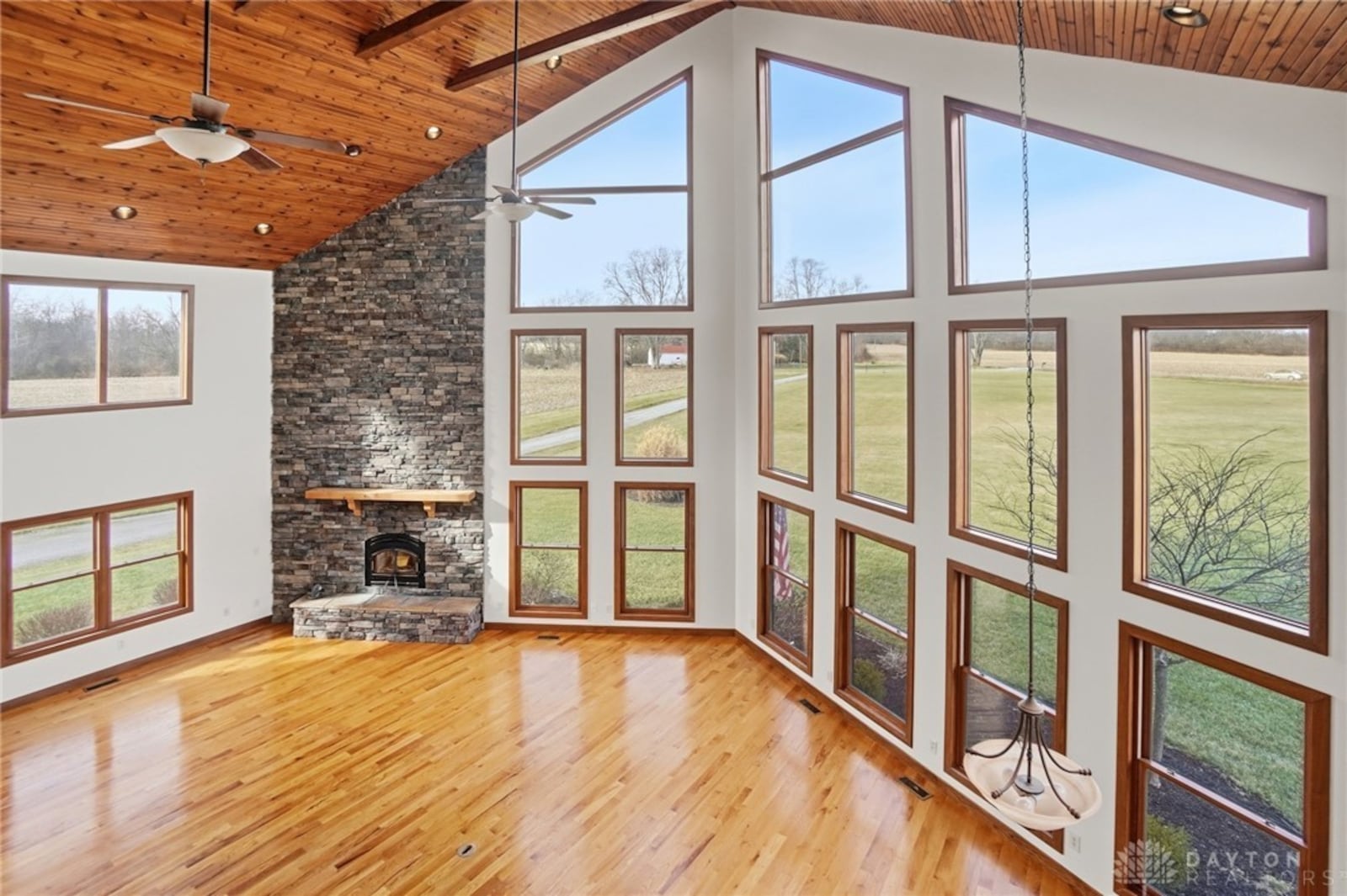 The two story great room has a beadboard ceiling, hardwood flooring, a floor to ceiling stacked stone fireplace with raised hearth and floor to ceiling windows on two sides. CONTRIBUTED