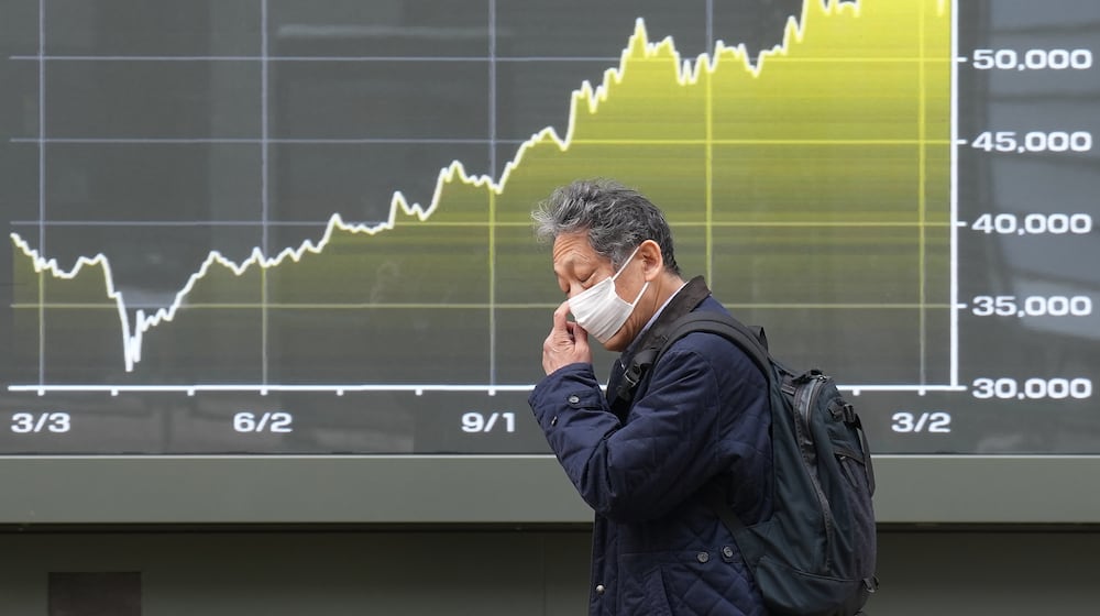 A person walks in front of an electronic stock board showing Japan's Nikkei index at a securities firm Friday, March 13, 2026, in Tokyo. (AP Photo/Eugene Hoshiko)