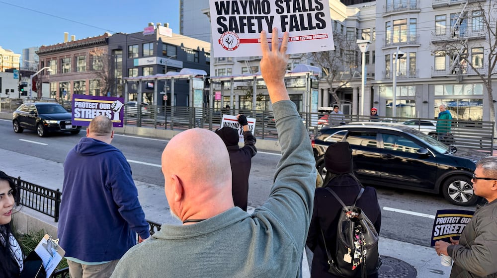 Demonstrators holds signs during a protest by Uber and Lyft drivers asking state regulators to take self-driving taxis off the streets due to safety concerns at the California Public Utilities Commission headquarters Friday, Jan. 9, 2026, in San Francisco. (AP Photo/Haven Daley)