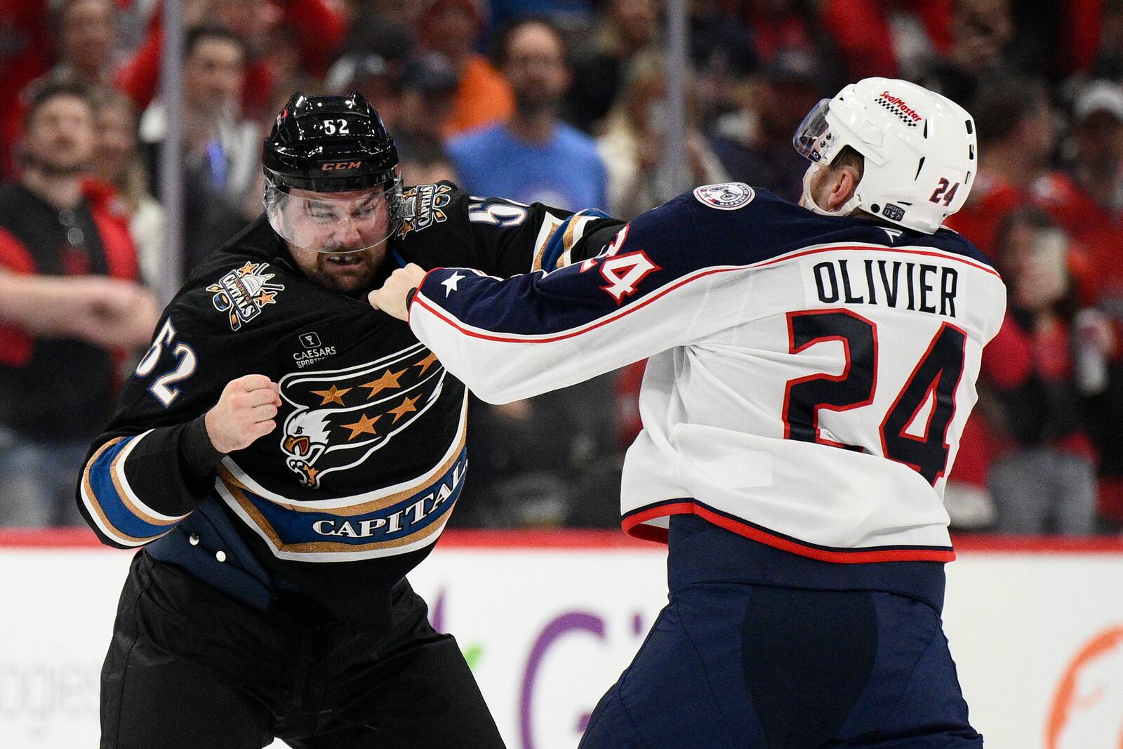 Washington Capitals defenseman Dylan McIlrath (52) and Columbus Blue Jackets right wing Mathieu Olivier (24) fight during the first period of an NHL hockey game, Sunday, April 13, 2025, in Washington. (AP Photo/Nick Wass)