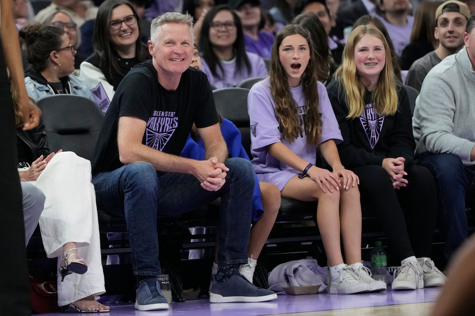 Golden State Warriors head coach Steve Kerr, foreground left, smiles during the second half of a WNBA basketball game between the Golden State Valkyries and the Los Angeles Sparks in San Francisco, Friday, May 16, 2025. (AP Photo/Jeff Chiu)