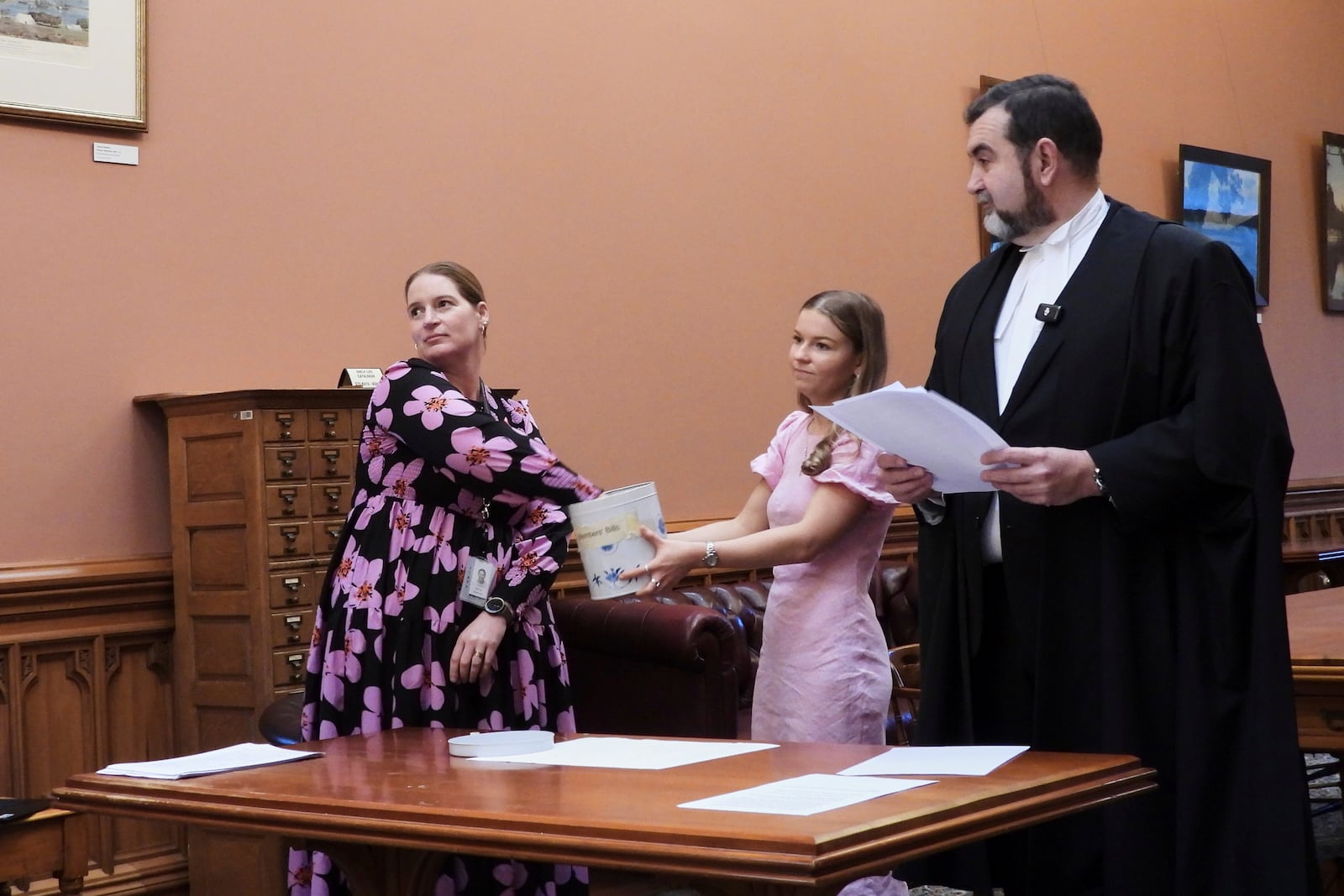 Parliamentary Service staffer Renee Beeson, left, draws a bingo token from the biscuit tin, observed by Chloe French and Clerk of the New Zealand House of Representatives David Wilson at Parliament in Wellington, New Zealand, Thursday, May 22, 2025. (AP Photo/Charlotte Graham-McLay)
