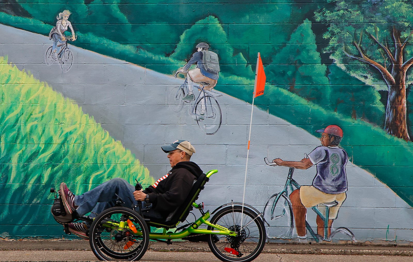 Diana Daniels, an employee of the Bicycle Stop on West 1st Street in Springfield, rides past the mural on the side of the business as she tries out a new motorized recumbent trike Monday, Oct. 16, 2023. BILL LACKEY/STAFF