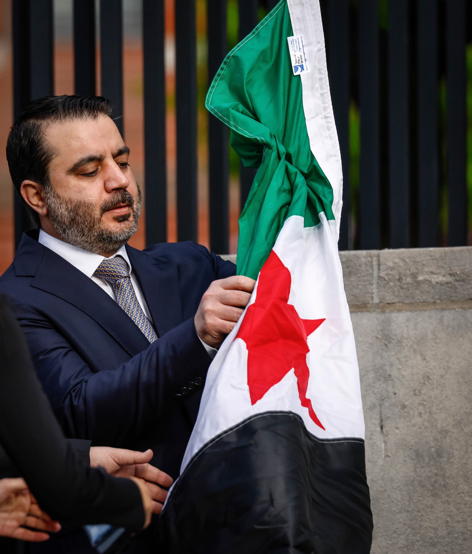 Syria's Foreign Minister Asaad Al-Shibani unfolds the Syrian Flag during a ceremony where the Syrian flag was added to the 100 flags flying in line at United Nations Headquarters on Friday, April 25, 2025. (AP Photo/Kena Betancur)