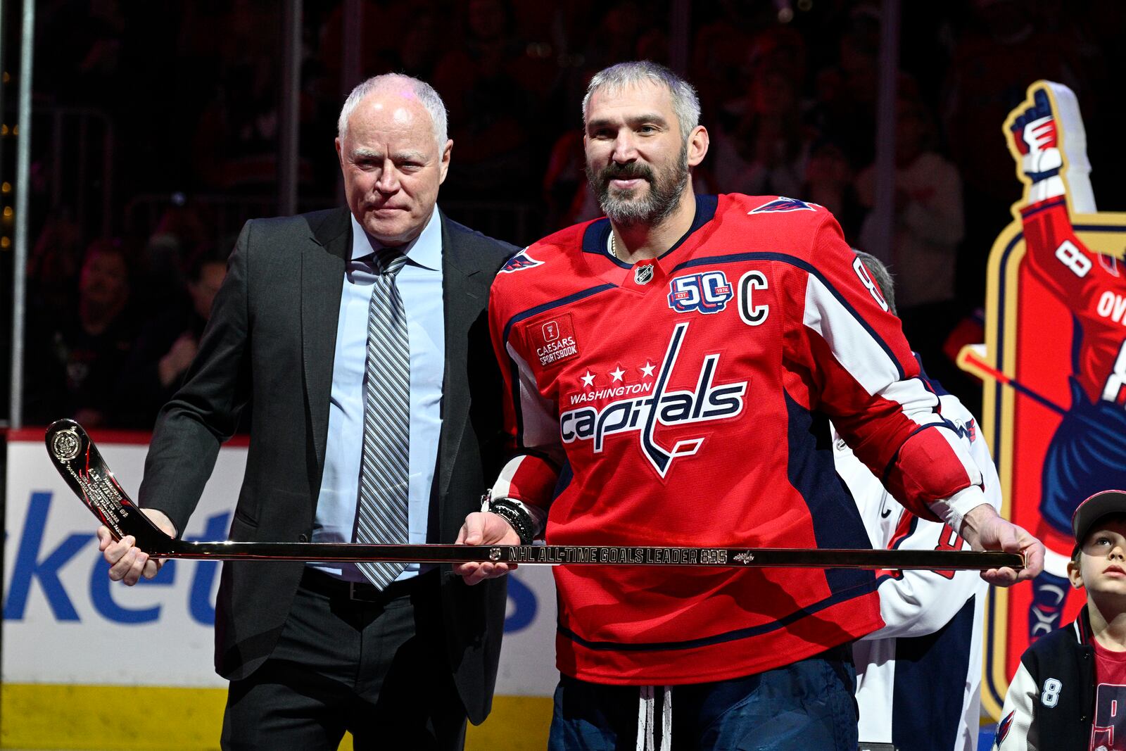Brian MacLellan, president of Washington Capitals hockey operations, left, poses with Capitals left wing Alex Ovechkin, right, after gifting him a gold stick as part of a ceremony to honor him for scoring 895 career NHL goals before an NHL hockey game against the Carolina Hurricanes, Thursday, April 10, 2025, in Washington. (AP Photo/Nick Wass)