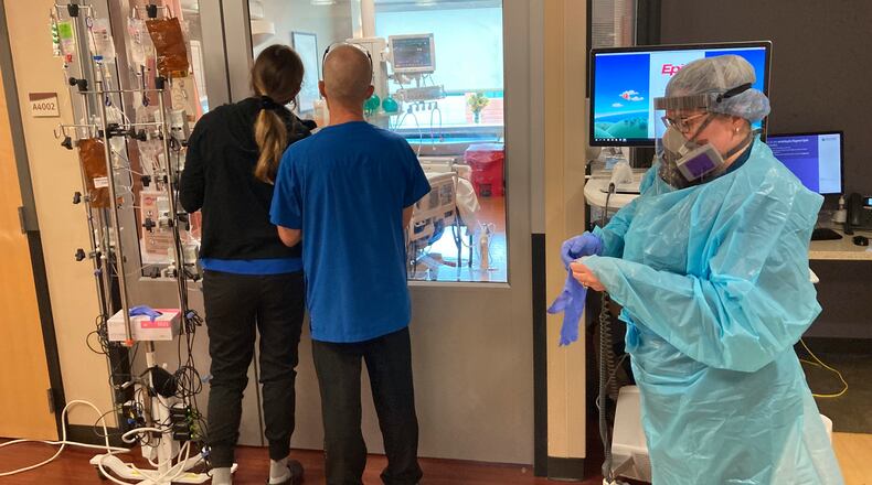 FILE - In this Aug. 20, 2021, file photo, two visitors peer into the room of a COVID-19 patient in the intensive care unit at Salem Hospital in Salem, Ore., as a nurse dons full protective gear before going into the room of another patient. Gov. Kate Brown announced Wednesday, Aug. 25, 2021, that the state has contracted with a medical staffing company to provide up to 500 health care workers to hospitals around the state to help respond to the surge in patients due to the delta variant. (AP Photo/Andrew Selsky, File)