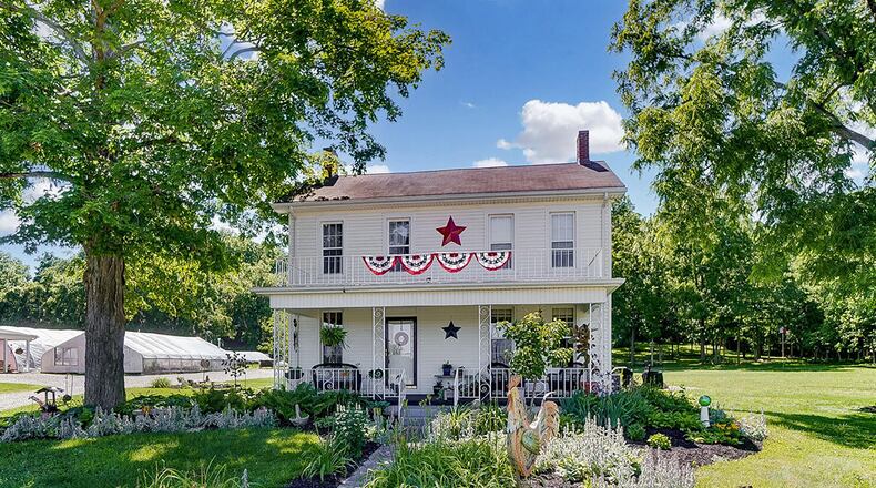 Spanning nearly 6 acres, the property includes the main 3-bedroom home as well as 2 barns, 3 greenhouses and a garden shed. the front of the farmhouse style home features a full, covered porch, multiple windows and a stone-paved driveway. CONTRIBUTED PHOTO