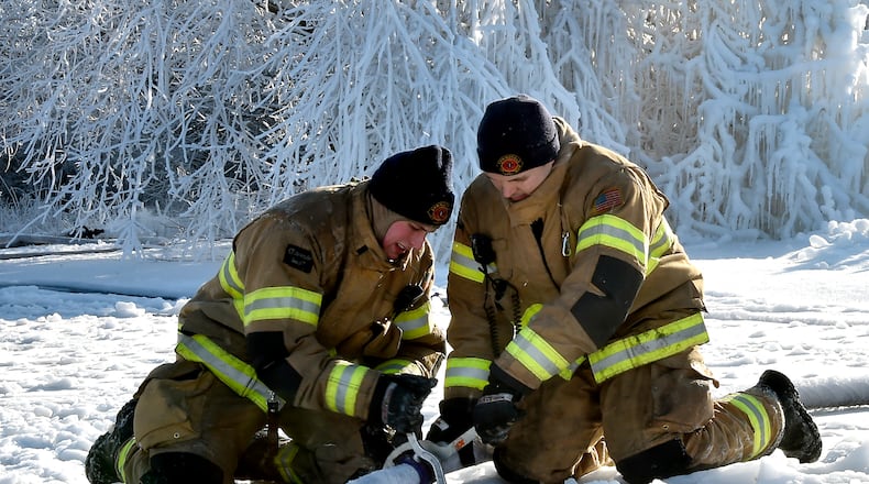 Members of the Springfield Fire Division try to break their fire hoses apart after they were coated with ice Wednesday morning following an overnight five alarm industrial fire in the 200 block of Monroe Street. Bill Lackey/Staff