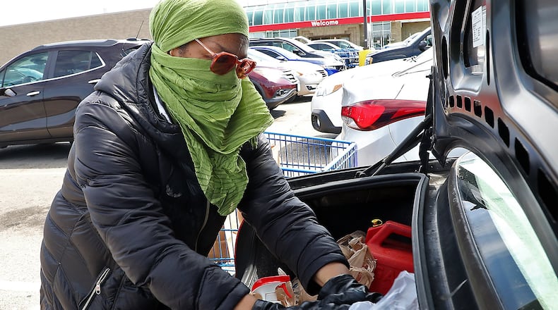 Ernnee Webber wears a scarf over her head and face and gloves as she puts her groceries in the trunk of her car Friday at Meijer in Springfield. Webber said she tried to find some medical masks but every place was sold out, so she made her own. BILL LACKEY/STAFF