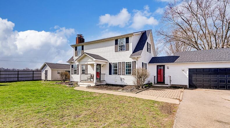 The front of the two story home features a covered concrete porch, two car attached garage with breezeway and a paver patio. There is a yard shed next to the home.