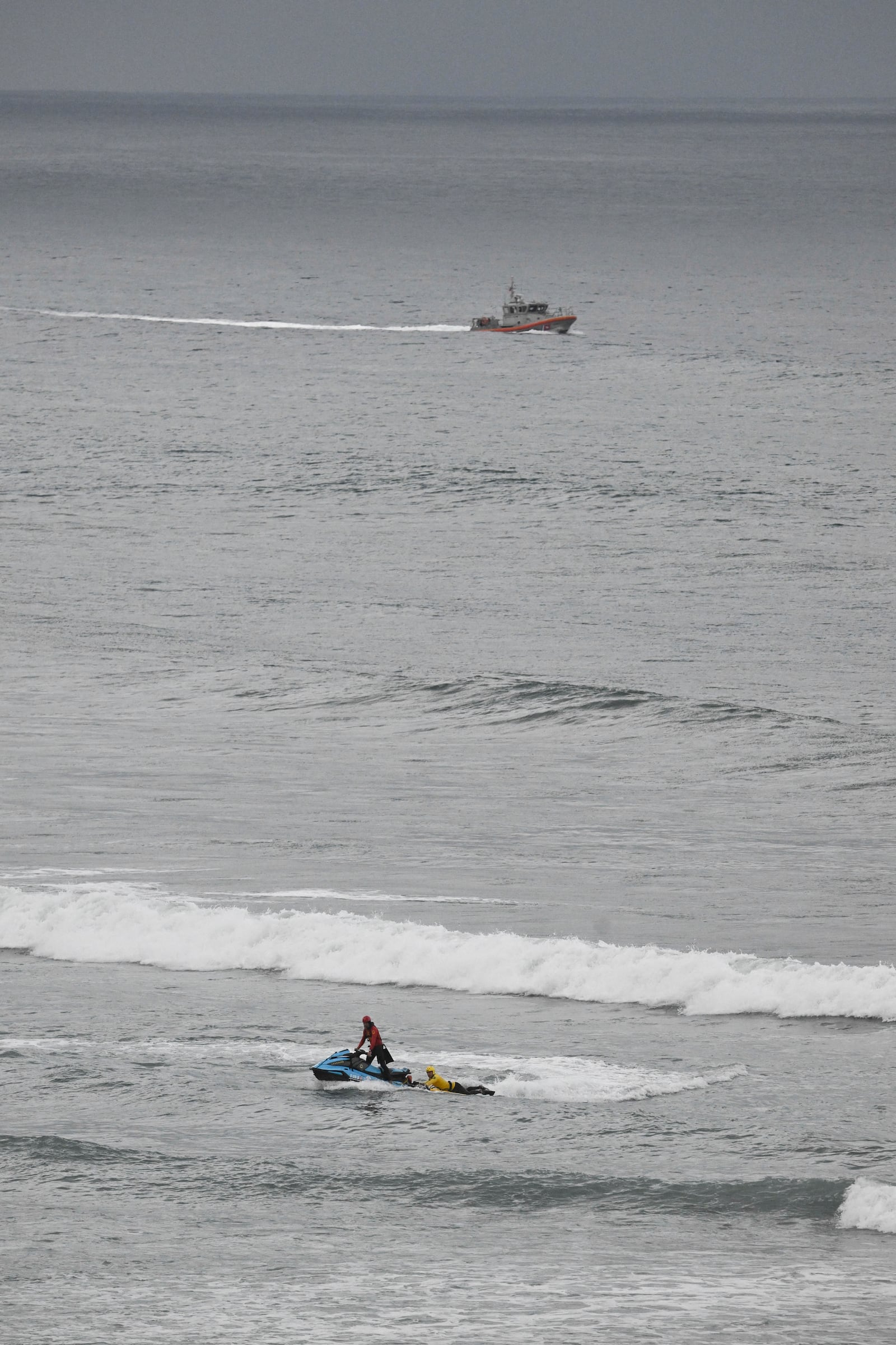 A U.S Coast Guard boat and lifeguards look for survivors after a boat capsized in the surf Friday, May. 5, 2025, in at Torrey Pines State beach in San Diego, Calif. (AP Photo/Denis Poroy)