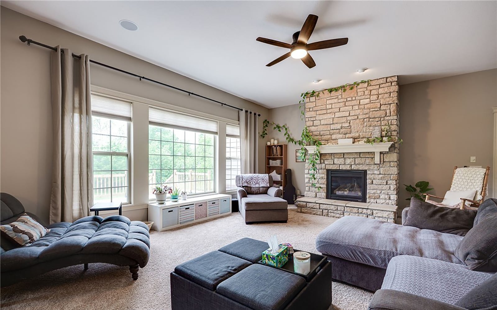 The great room has a stacked stone fireplace, neutral carpeting, a ceiling fan and recessed lighting. CONTRIBUTED