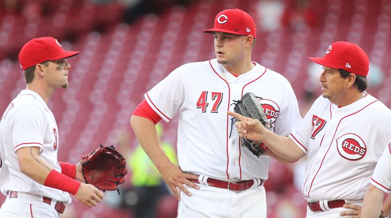 Reds starter Sal Romano, center, is visited by catcher Tucker Barnhart, far right, pitching coach Mack Jenkins, second from right, and Scooter Gennett during a game against the Cardinals on Thursday, April 12, 2018, at Great American Ball Park in Cincinnati. David Jablonski/Staff