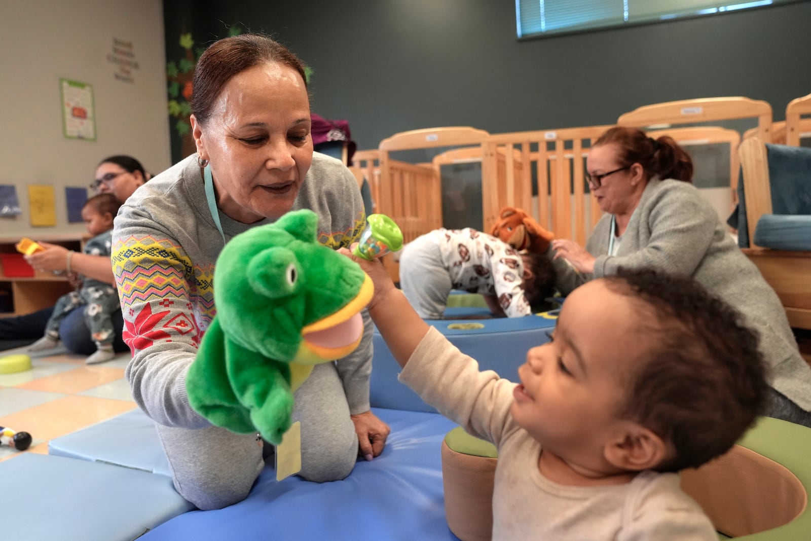 FILE - Volunteer Ydalina Luna Sosa, 62, of Providence, R.I., front left, uses a frog puppet for entertainment while supervising 10-month-old Leo Morgenweck, front right, in an early childcare program at Federal Hill House, Nov. 12, 2024, in Providence, R.I. (AP Photo/Steven Senne, File)