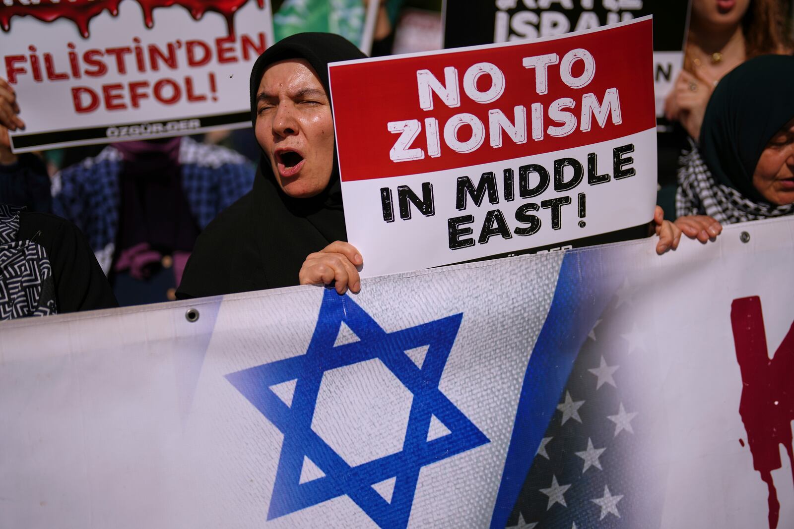 People shout slogans during an anti Israel protest in Istanbul, Turkey, Saturday, June 21, 2025. The board on the left reads in Turkish: "Get out of Palestine". (AP Photo/Francisco Seco)