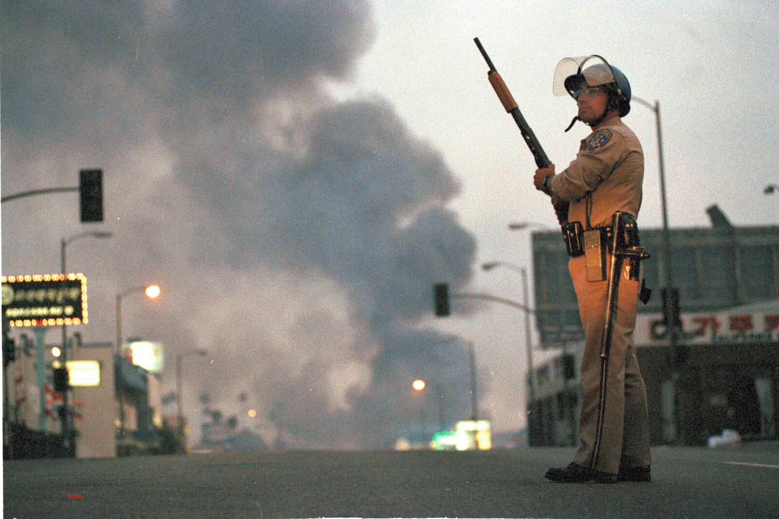 FILE - A California Highway Patrol officer stands guard at Ninth Street and Vermont Avenue in Los Angeles as smoke rises from a fire further down the street, April 30, 1992. (AP Photo/David Longstreath, file)