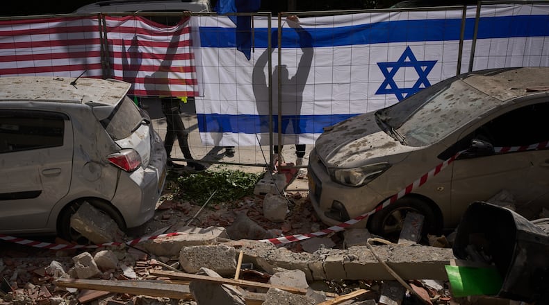Israeli authorities hang Israeli and U.S. flags at the site struck by an Iranian missile that killed two people, in Ramat Gan, Israel, Wednesday, March 18, 2026. (AP Photo/Oded Balilty)