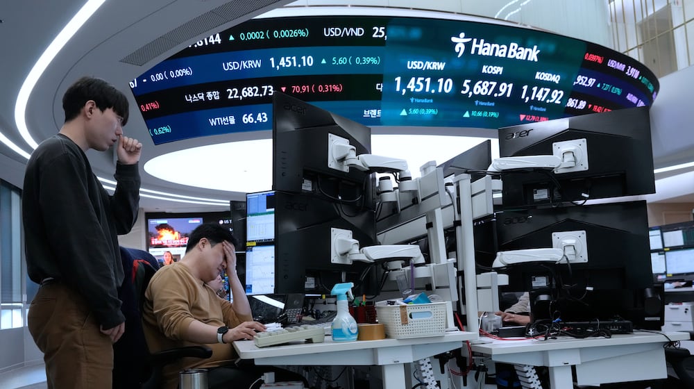 Currency traders work near a screen showing the Korea Composite Stock Price Index (KOSPI), top center, and the foreign exchange rate between U.S. dollar and South Korean won, top center left, at the foreign exchange dealing room of the Hana Bank headquarters in Seoul, South Korea, Friday, Feb. 20, 2026. (AP Photo/Ahn Young-joon)