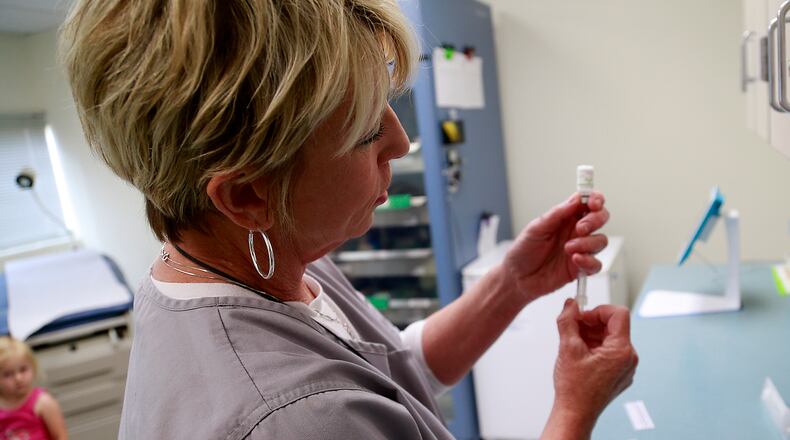 Kellie Adams, a nurse at the Clark County Combined Health District, gets a shot ready for Briley Wilson, in the background, Wednesday. BILL LACKEY/STAFF