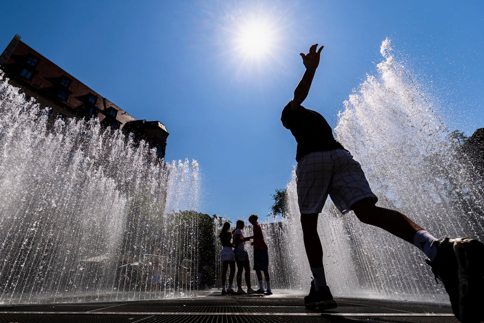 Young people walk through the water installation "Hexagonal Water Pavilion" by Danish artist Jeppe Hein in front of the Neues Museum in Nuremberg, Germany, Wednesday, July 2, 2025. (Daniel Karmann/dpa via AP)