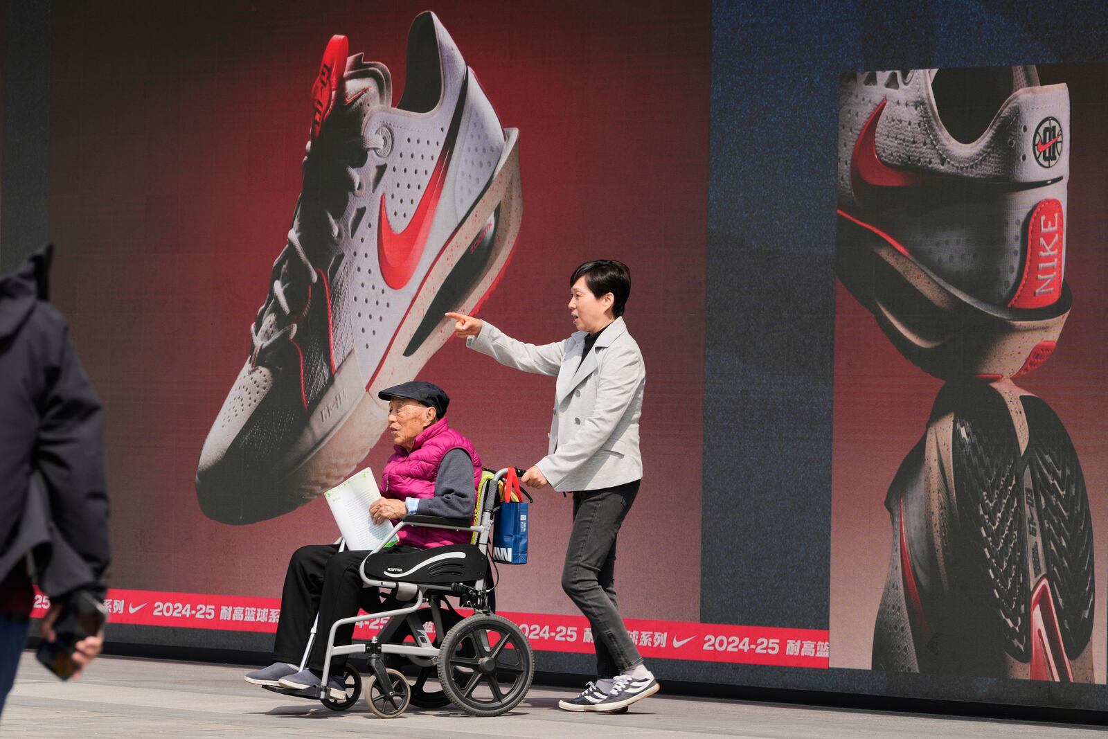 A woman pushes an elderly man past a Nike store at a mall in Beijing, Wednesday, May 7, 2025. (AP Photo/Ng Han Guan)