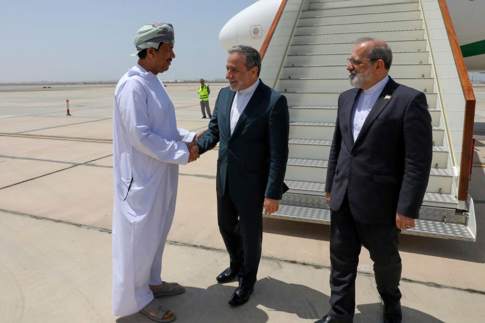 In this photo released by the Iranian Foreign Ministry, Iranian Foreign Minister Abbas Araghchi, center, is welcomed by an unidentified Omani official upon his arrival at Muscat, Oman, for negotiations with U.S. Mideast envoy Steve Witkoff, as Iranian Ambassador to Oman Mousa Farhang stands at right, Sunday, May 11, 2025. (Iranian Foreign Ministry via AP)