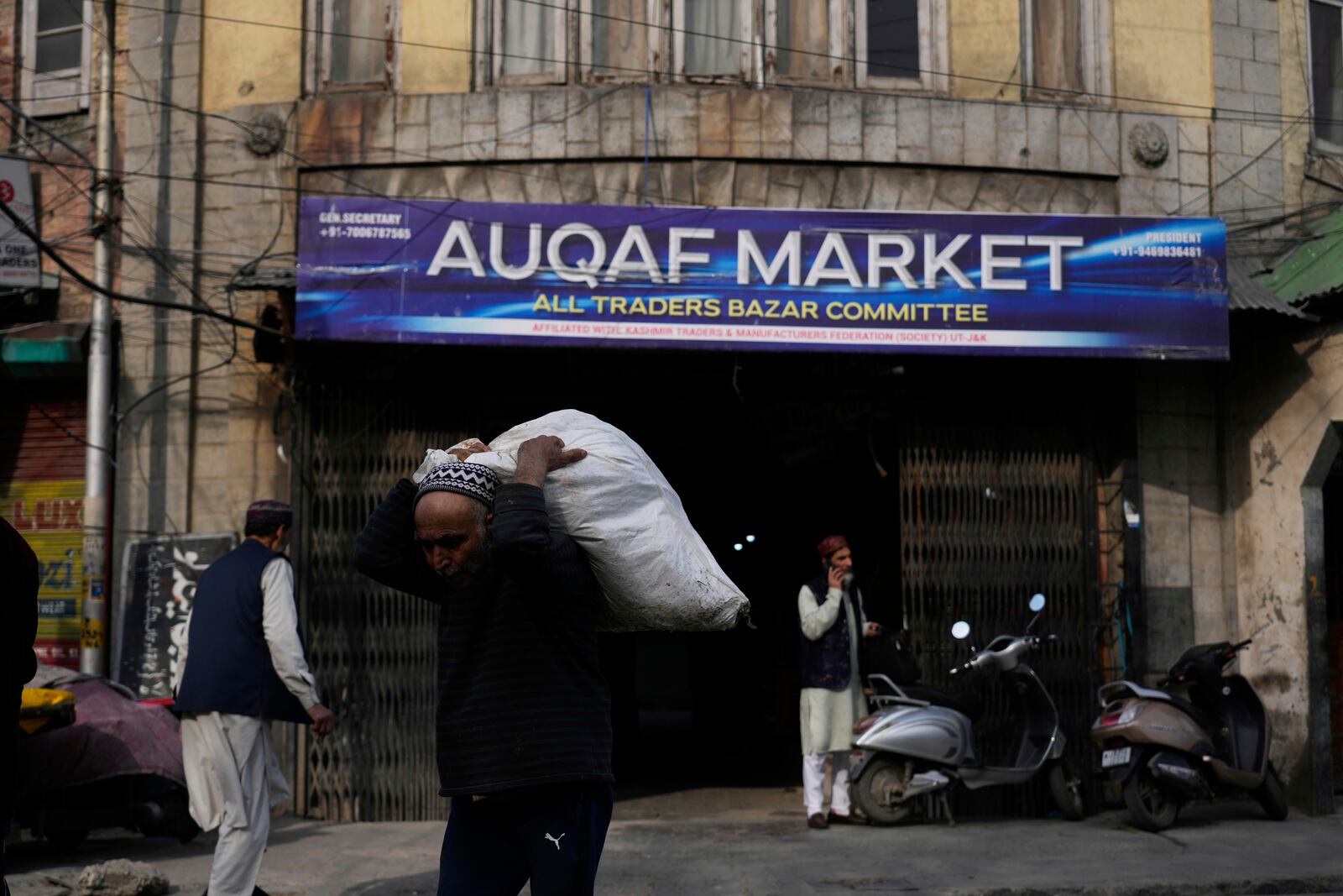 An elderly Kashmiri man carries a plastic sack filled with fabric as he walks outside the Auqaf Market in Srinagar, Indian controlled Kashmir, Wednesday, April 2, 2025. (AP Photo/Mukhtar Khan)