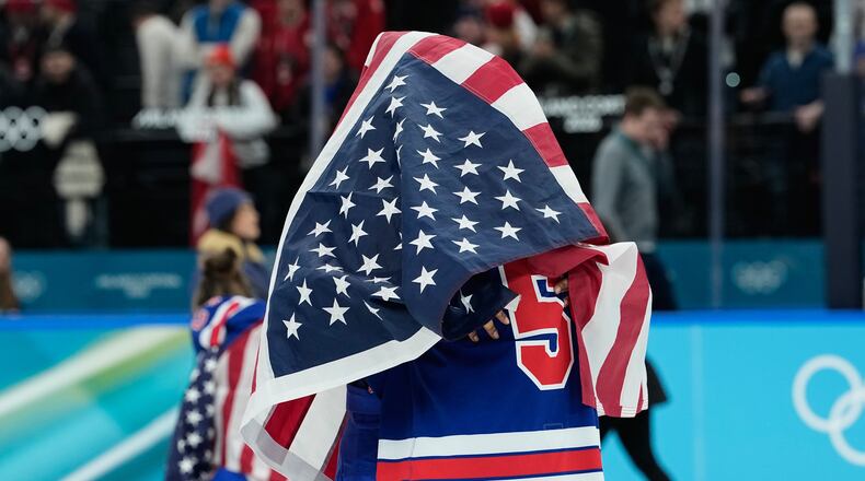 United States' Megan Keller (5), covered in the U.S. flag, gets a hug from a teammate after the United States' women's ice hockey team stand after being presented with the gold medals at the 2026 Winter Olympics, in Milan, Italy, Thursday, Feb. 19, 2026. (AP Photo/Petr David Josek)