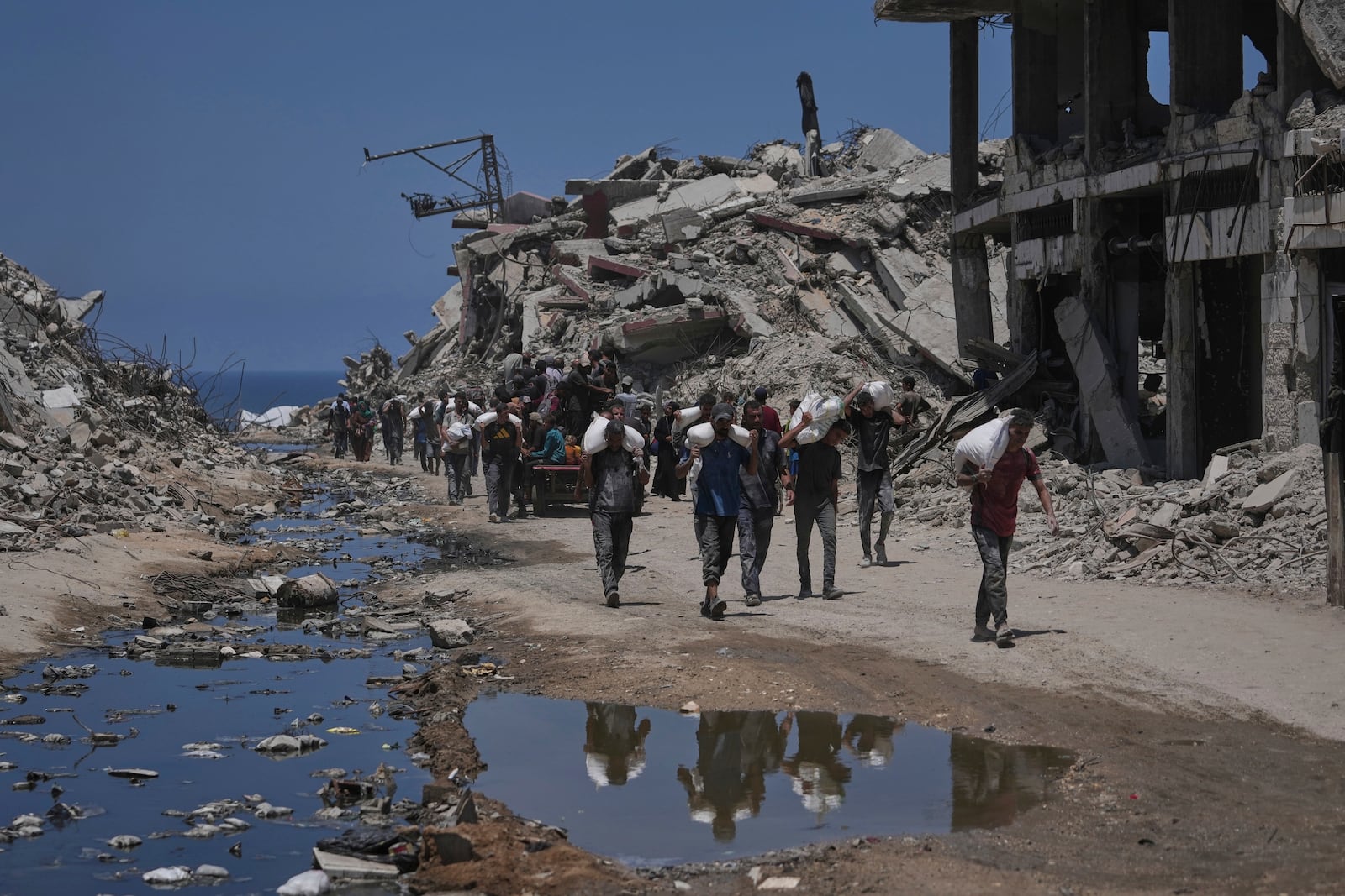 Palestinians carry sacks of flour unloaded from a humanitarian aid convoy that reached Gaza City from the northern Gaza Strip, Tuesday, July 22, 2025. (AP Photo/Jehad Alshrafi)