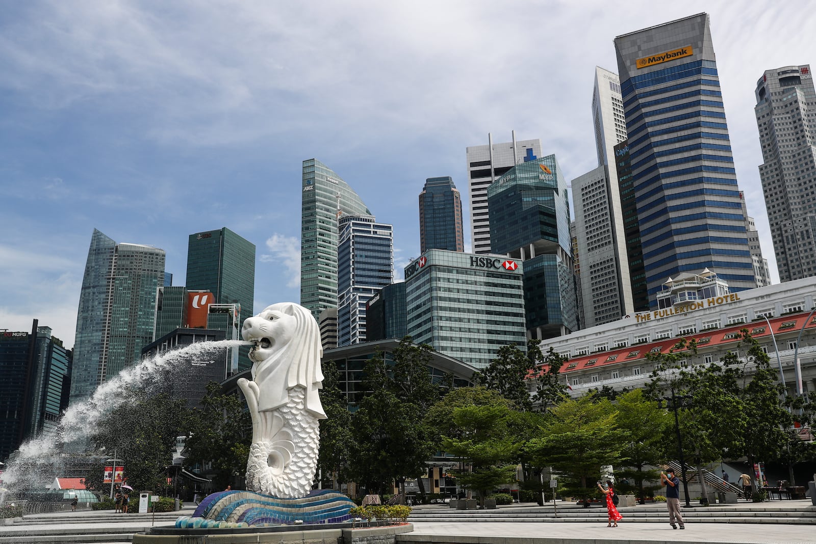 FILE - People are dwarfed against the financial skyline as they take photos of the Merlion statue along the Marina Bay area in Singapore, on June 30, 2020. (AP Photo/Yong Teck Lim, File)