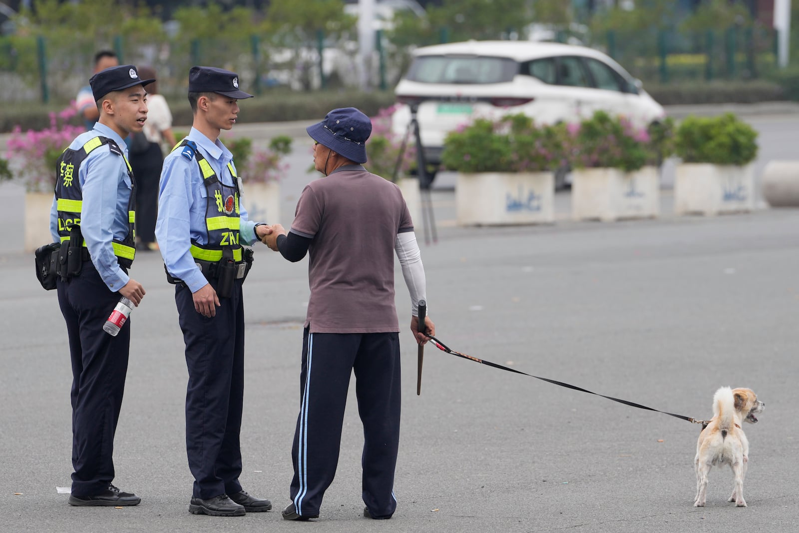 FILE - Police officers talk with a man walking his dog in front of the "Zhuhai People's Fitness Plaza" where a man deliberately rammed his car into people exercising at the sports center, killing some and injuring others in Zhuhai, southern China's Guangdong province on Nov. 13, 2024. (AP Photo/Ng Han Guan, File)