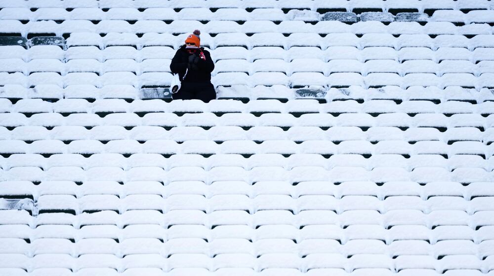 A fan sits in the stadium seats covered in snow before an NFL football game between the Cincinnati Bengals and the Baltimore Ravens, Sunday, Dec. 14, 2025, in Cincinnati. (AP Photo/Carolyn Kaster)