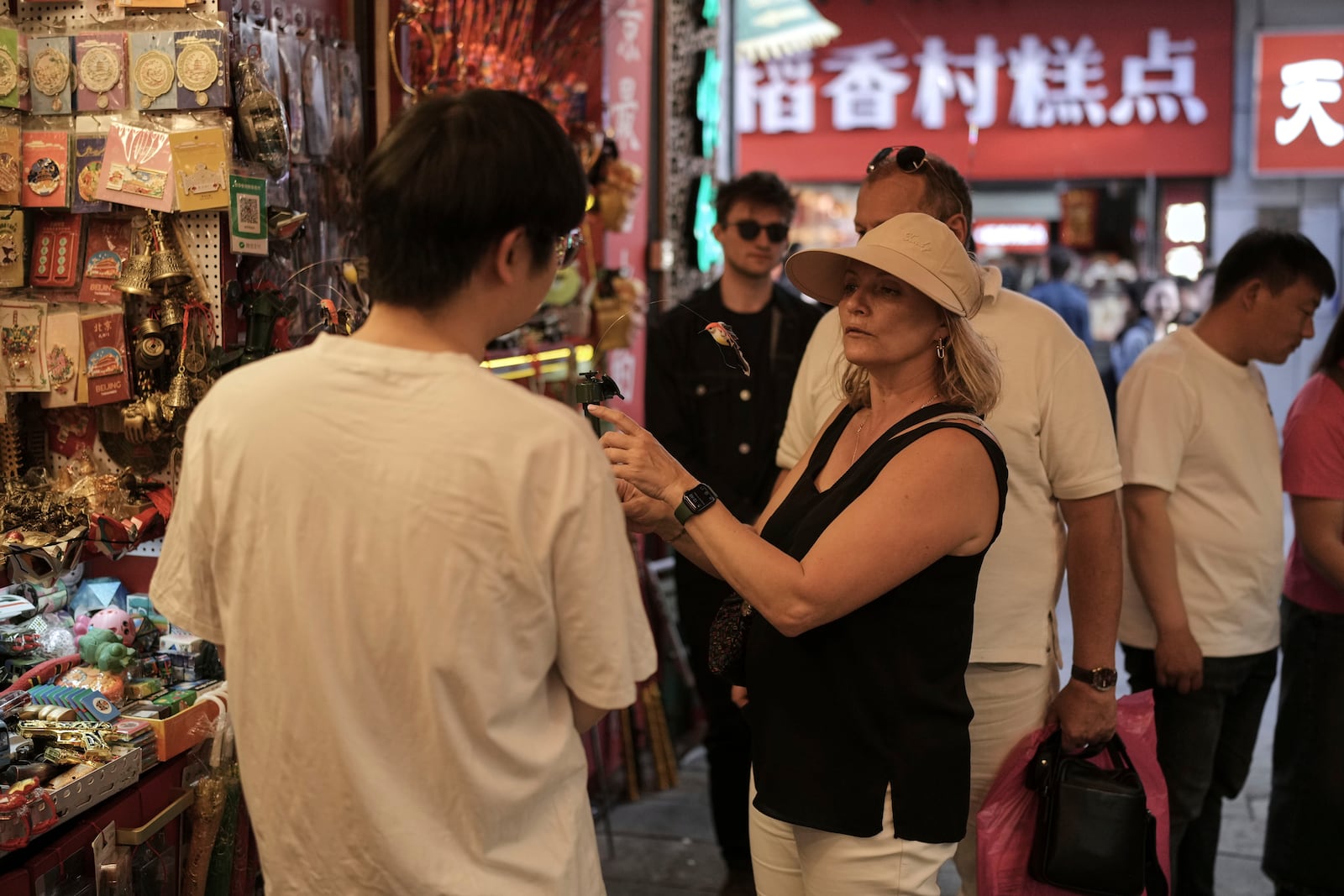 A tourist couple bargain price with a vendor at a souvenir store as they visit Qianmen pedestrian shopping street in Beijing, Sunday, April 27, 2025. (AP Photo/Andy Wong)