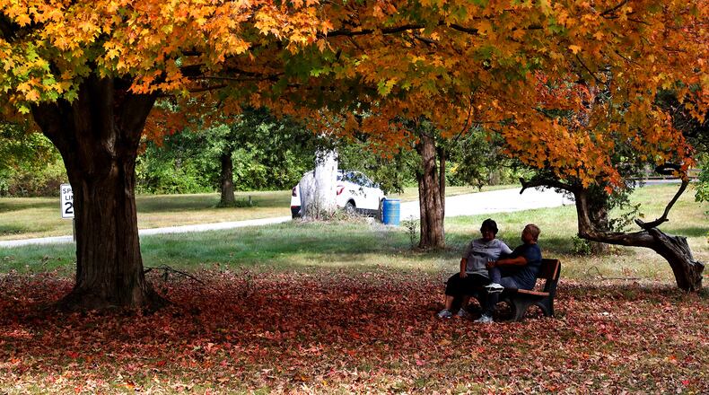Two women relax on a bench under a canopy of orange and yellow at George Rogers Clark Park Friday. The trees in the park will make a colorful backdrop for the Haunted Halloween Drive-Thru Friday. BILL LACKEY/STAFF