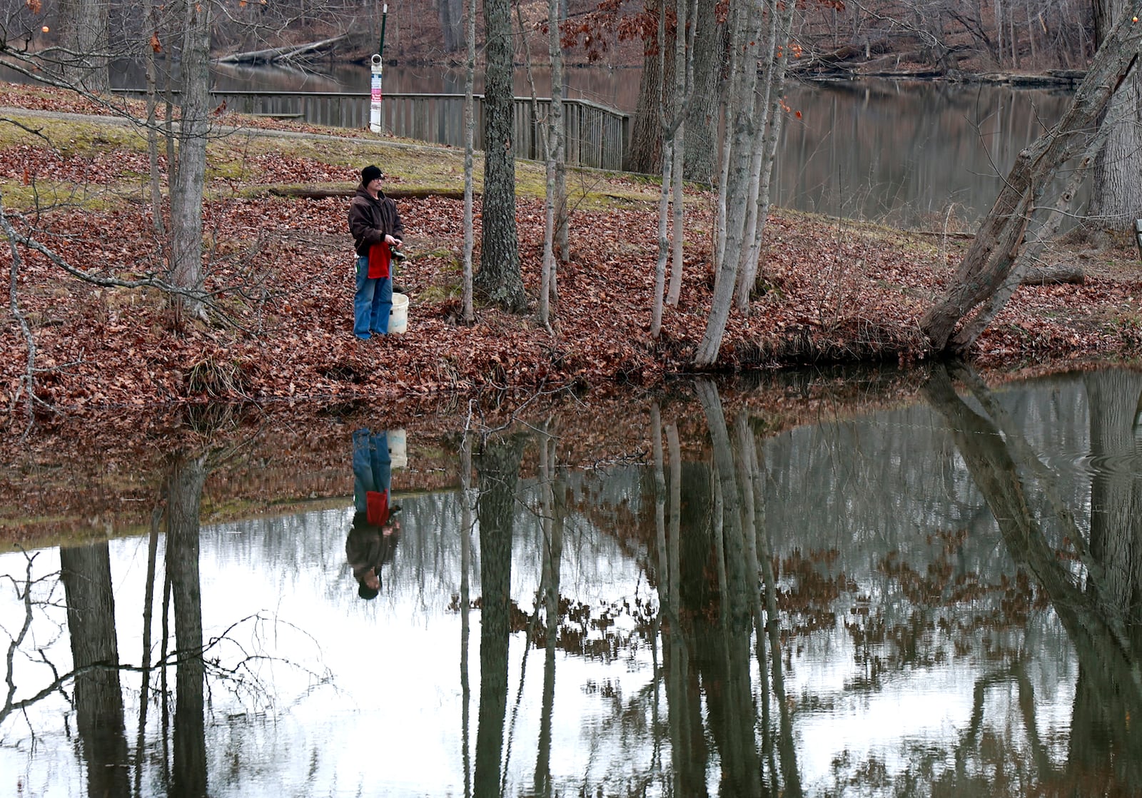 A fisherman is reflected in the water at Hosterman Lake in George Rogers Clark Park as he tries his luck near the spillway Wednesday, Jan. 18, 2023. BILL LACKEY/STAFF