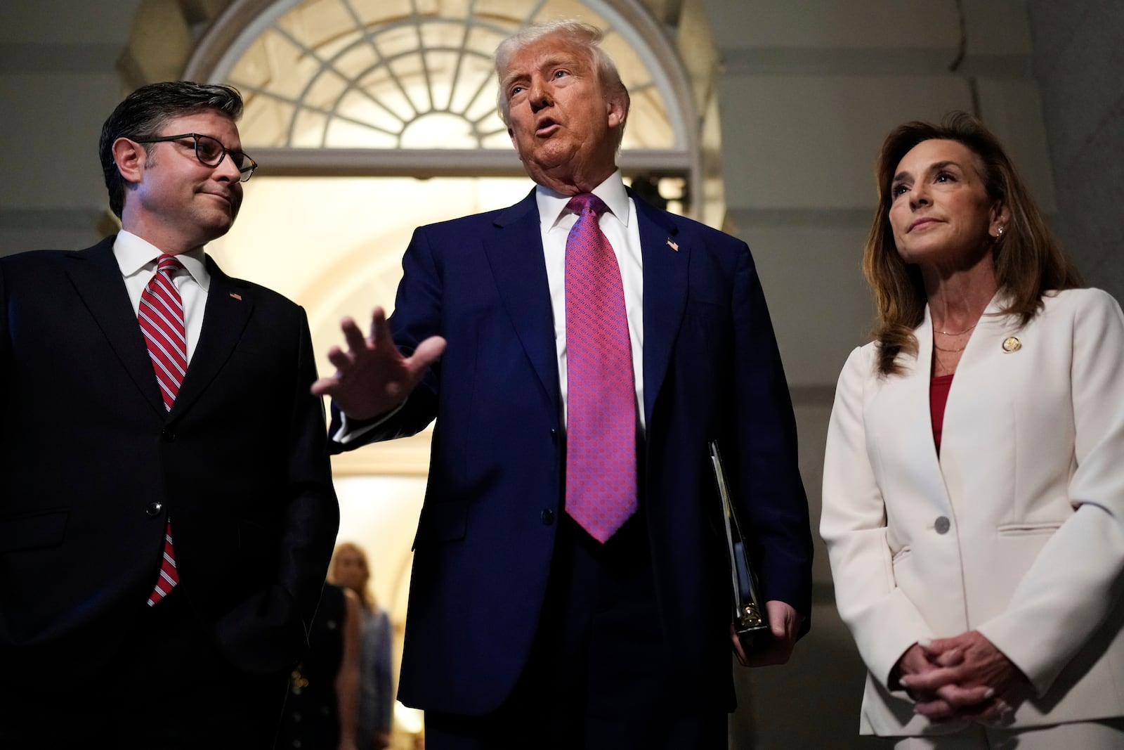President Donald Trump, center, surrounded by Speaker of the House Mike Johnson, R-La., and Rep. Lisa McClain, R-Mich., speaks to reporters before a House Republican conference meeting, Tuesday, May 20, 2025, at the U.S. Capitol in Washington. (AP Photo/Julia Demaree Nikhinson)