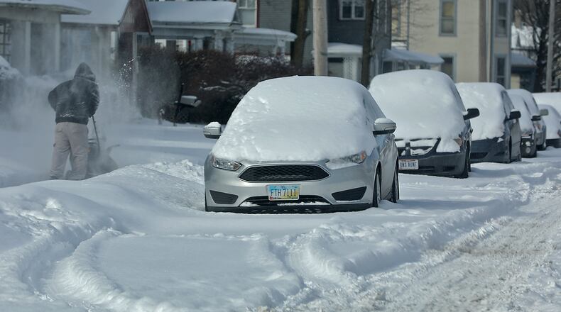 A man cleans off the sidewalk along a row of cars, buried in the snow, on East Madison Street in Springfield. BILL LACKEY/STAFF