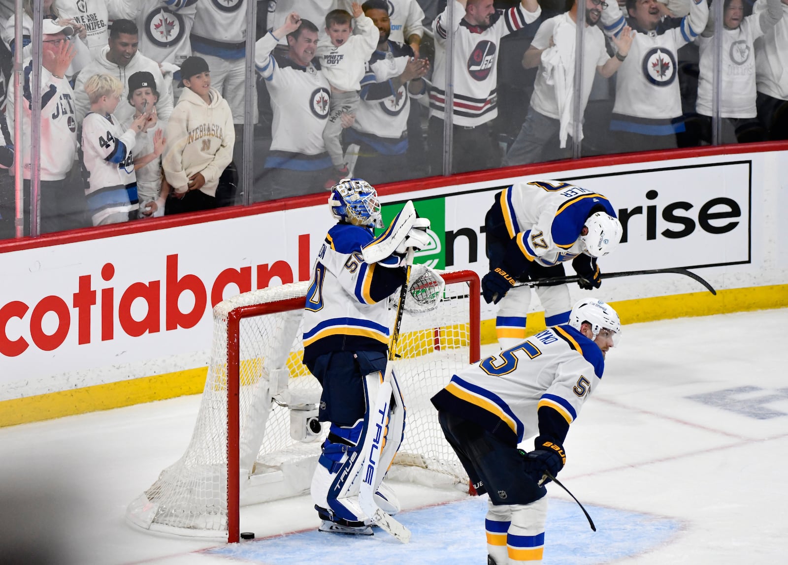 St. Louis Blues' goaltender Jordan Binnington (50), Colton Parayko (55) and Cam Fowler (17) react as the Winnipeg Jets celebrate their game-winning goal in the second overtime period of Game 7 in an NHL hockey first-round playoff series in Winnipeg, Manitoba, Sunday, May 4, 2025. (Fred Greenslade/The Canadian Press via AP)
