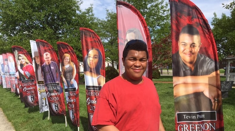 Tevin Pruitt stands next to his flag in Settlers’ Park in Enon. The flags are recognizing high school graduates in Mad River Twp., Enon and Green Twp. PAM COTTREL/CONTRIBUTOR