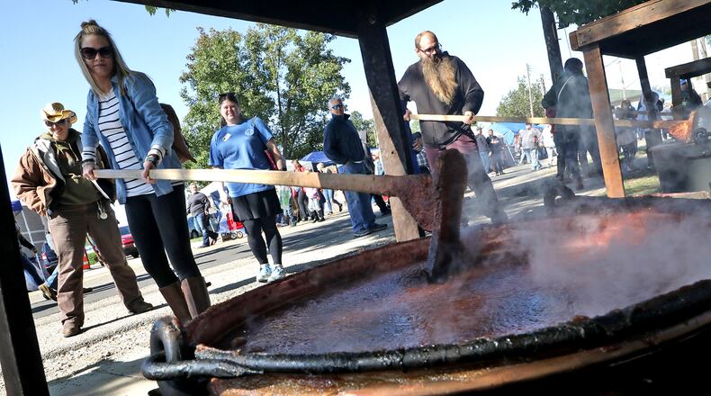 Festival attendees take a turn at stirring one of the giant kettles of apple butter cooking over an open fire at the Enon Apple Butter Festival Saturday. People took turns stirring the apple butter as it cooked throughout the day. Once the apple butter is finished cooking, its quickly canned and sold to the long line of people waiting. This year's festival will be held on Oct. 9 and 10. BILL LACKEY/STAFF