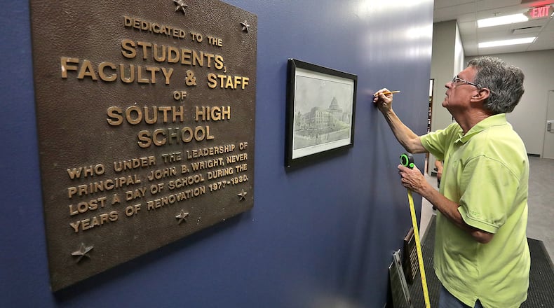 Don McKanna, one of the owners of Frame Haven, hangs old pictures and plaques from Springfield City School's past in the lobby of John Legend Theater Friday. BILL LACKEY/STAFF