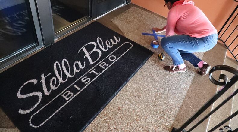 An employee at Stella Bleu Bistro puts X's on the floor of the restaurant to ensure social distancing on July 10. BILL LACKEY/STAFF