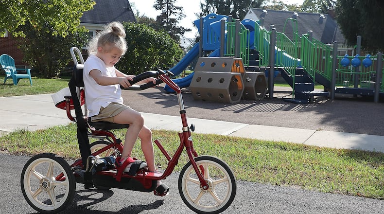 Lainey Wilson peddles a tricycle around the new paved walking path at the Mercy Health’s Pediatric Rehab playground Monday. BILL LACKEY/STAFF