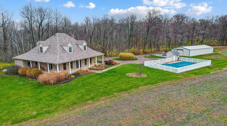The Cape Cod style brick home has a wraparound covered porch, in ground pool and detached barn with four garages.