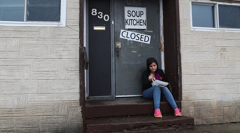 Kaylee Lucero eats a free meal on the front steps of the Springfield Soup Kitchen Wednesday. Due to the coronavirus, the Springfield Soup Kitchen is not allowed to open, so they got Kim and her husband, Fred, to park their food truck in the parking lot across the street from the soup kitchen and are feeding people outdoors. BILL LACKEY/STAFF