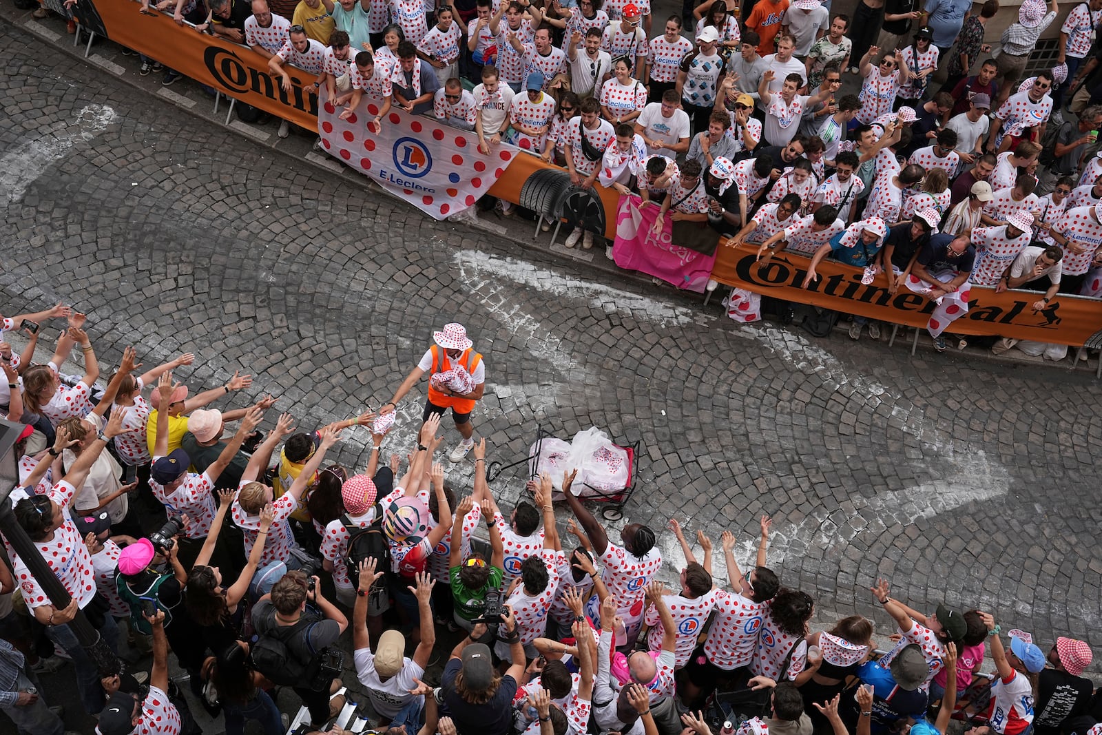 A man distributes publicity items to cycling fans in a packed street of the Montmartre district during the last stage of the Tour de France cycling race between Mantes-la-Ville and Paris, Sunday, July 27, 2025 in Paris (AP Photo/Laurent Cipriani)
