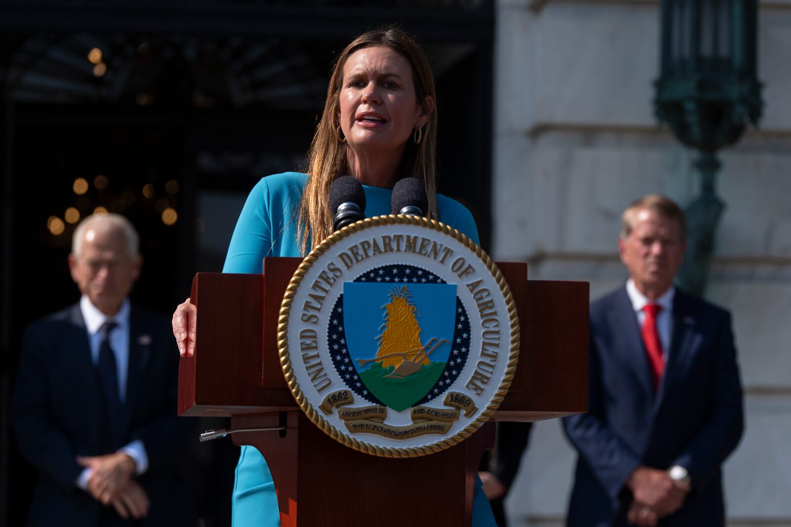 Arkansas Gov. Sarah Huckabee Sanders, center, with White House trade counselor Peter Navarro, left, and Nebraska Gov. Jim Pillen, right, speaks during a news conference at the Department of Agriculture to rollout the USDA'S National Farm Security Action Plan and discuss actions being taken to protect American agriculture from foreign threats in Washington, Tuesday, July 8, 2025. (AP Photo/Manuel Balce Ceneta)