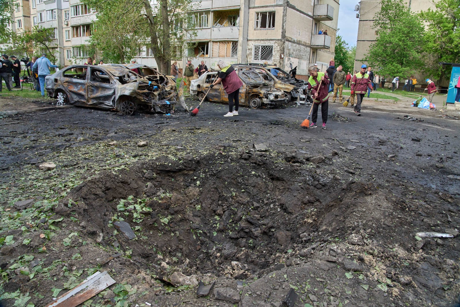 Municipal workers clean up near burnt cars and a crater made by a drone in the residential area following Russia's air raid in Kyiv, Ukraine, Sunday, May 4, 2025. (AP Photo/Efrem Lukatsky)